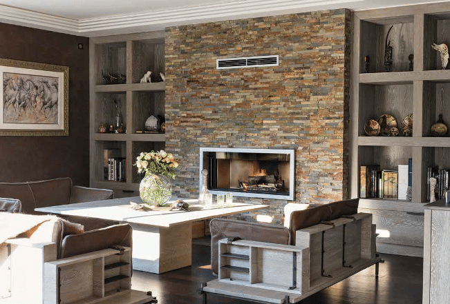 Encadré par deux grandes niches bibliothèque en chêne cérusé, le mur de la cheminée est ici habillé de barrettes d’ardoise oxydée de 10 cm d’épaisseur.