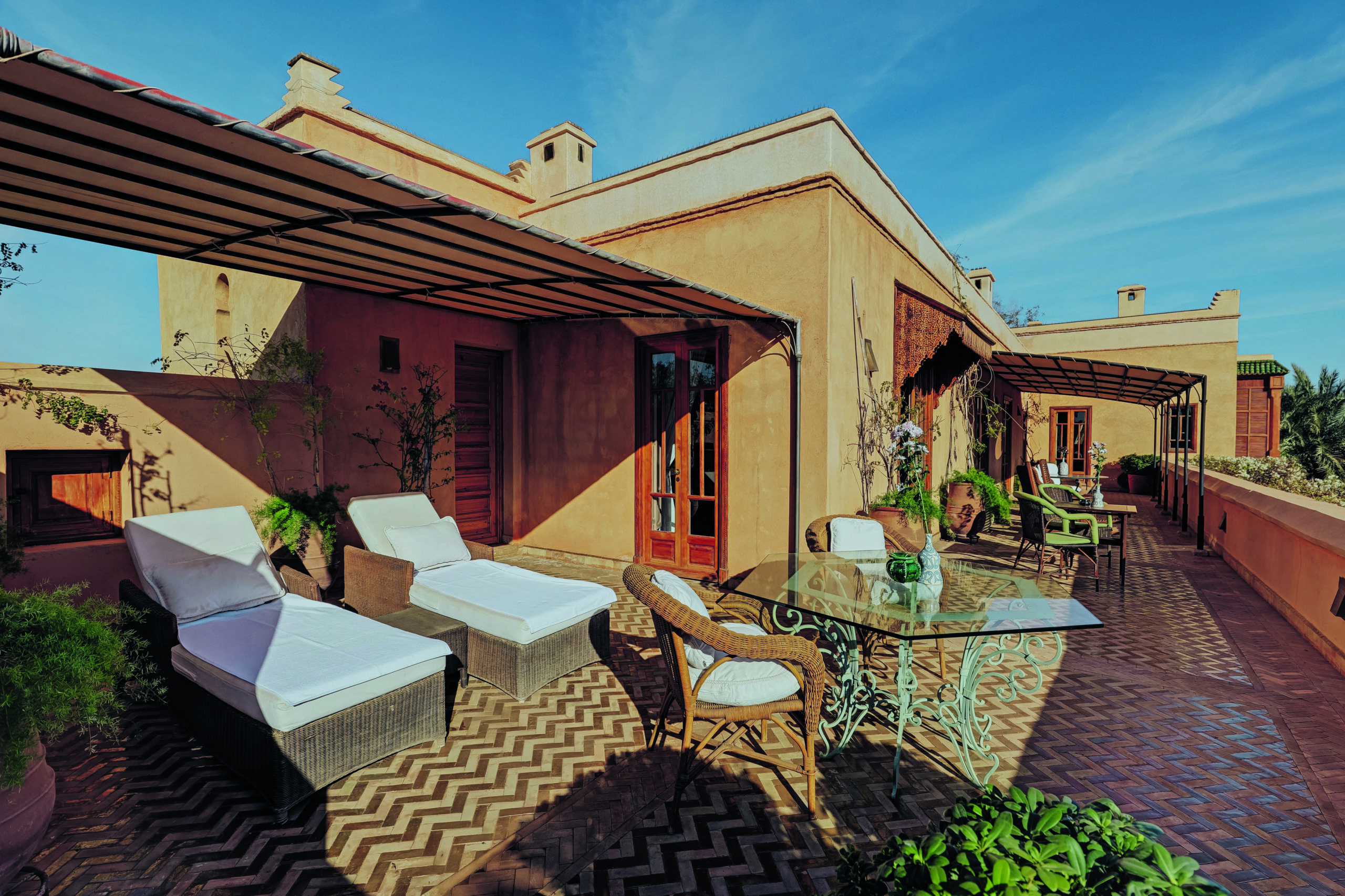 Terrasse d’hôtel avec mobilier extérieur, transats et table en fer forgé dans une architecture de style marocain sous ciel bleu