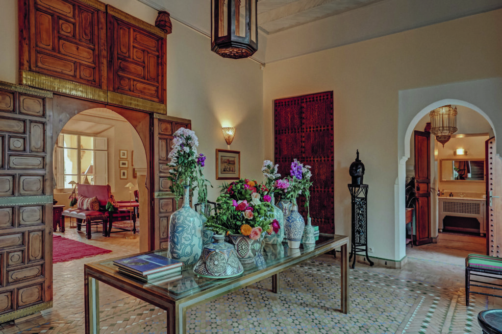 Intérieur d’hôtel avec décoration marocaine, arches sculptées, mobilier traditionnel et grande table fleurie dans un riad élégant