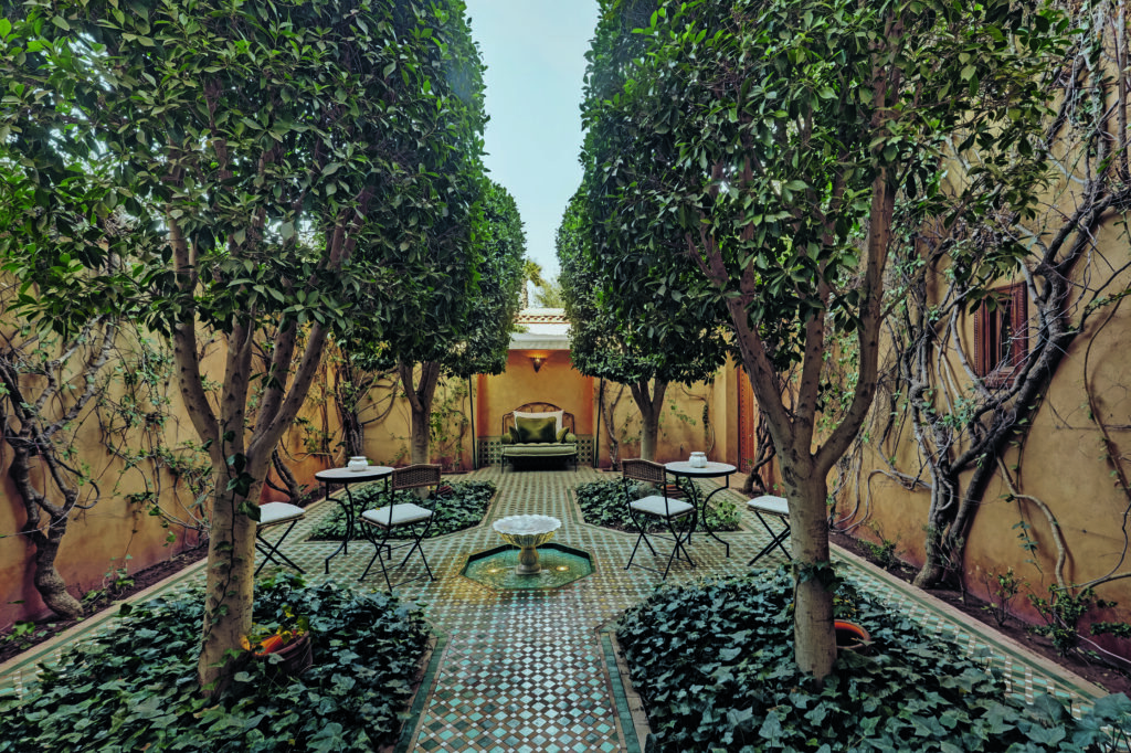 Patio de riad marocain avec jardin intérieur, fontaine centrale, arbres et mosaïque traditionnelle dans une ambiance paisible