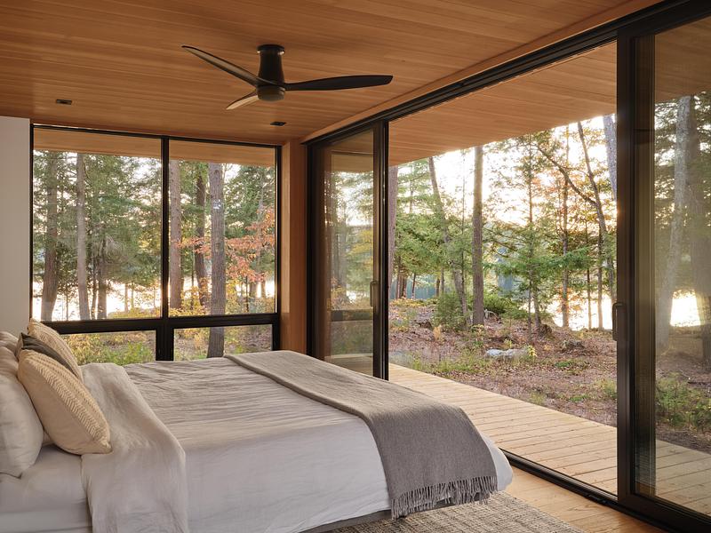Chambre minimaliste avec vue panoramique sur la nature, baies vitrées et ambiance chaleureuse en bois