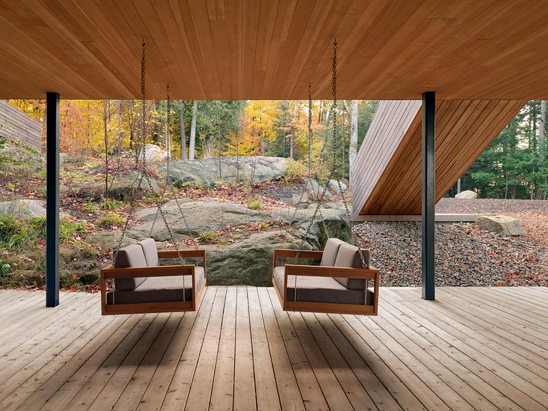 Terrasse en bois avec fauteuils suspendus face à un paysage naturel de roches et forêt au Canada