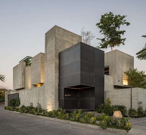 Façade en béton brut d’un studio d’architecture au Mexique avec arbre en arrière-plan et volumes minimalistes