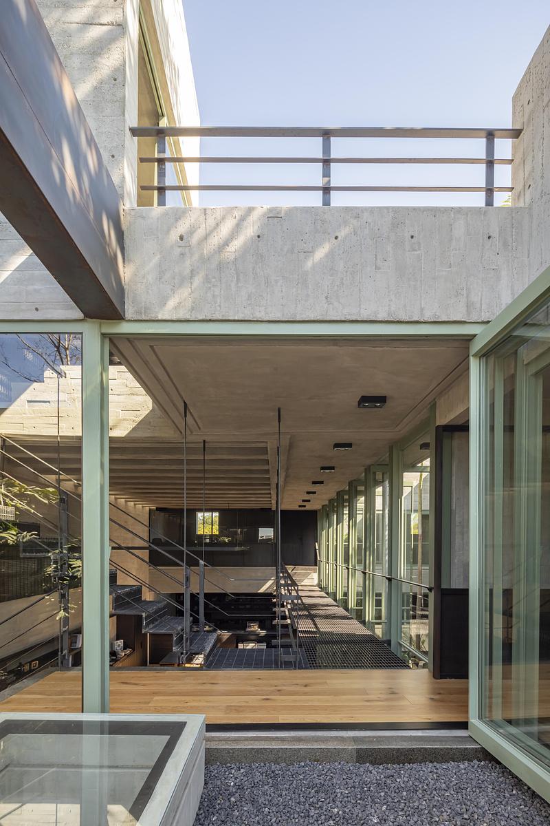 Passerelle intérieure en béton et acier avec structure verte et grandes baies vitrées dans un studio d’architecture au Mexique