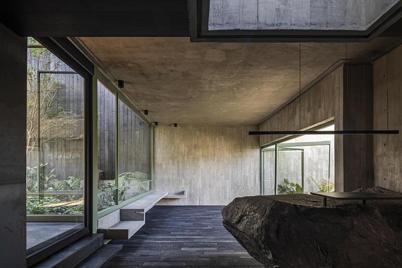 Intérieur de studio d’architecture en béton brut avec grandes baies vitrées et patio végétalisé au Mexique