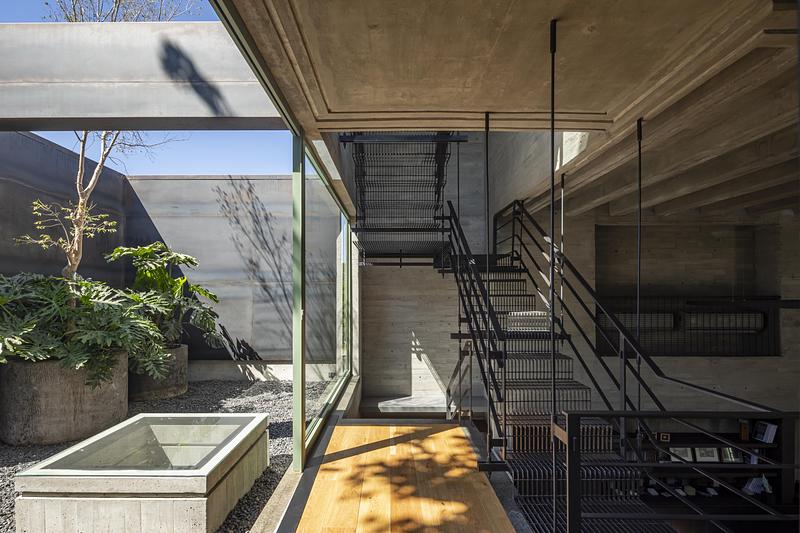 Escalier métallique dans un studio d’architecture avec patio intérieur, béton brut et grandes baies vitrées au Mexique