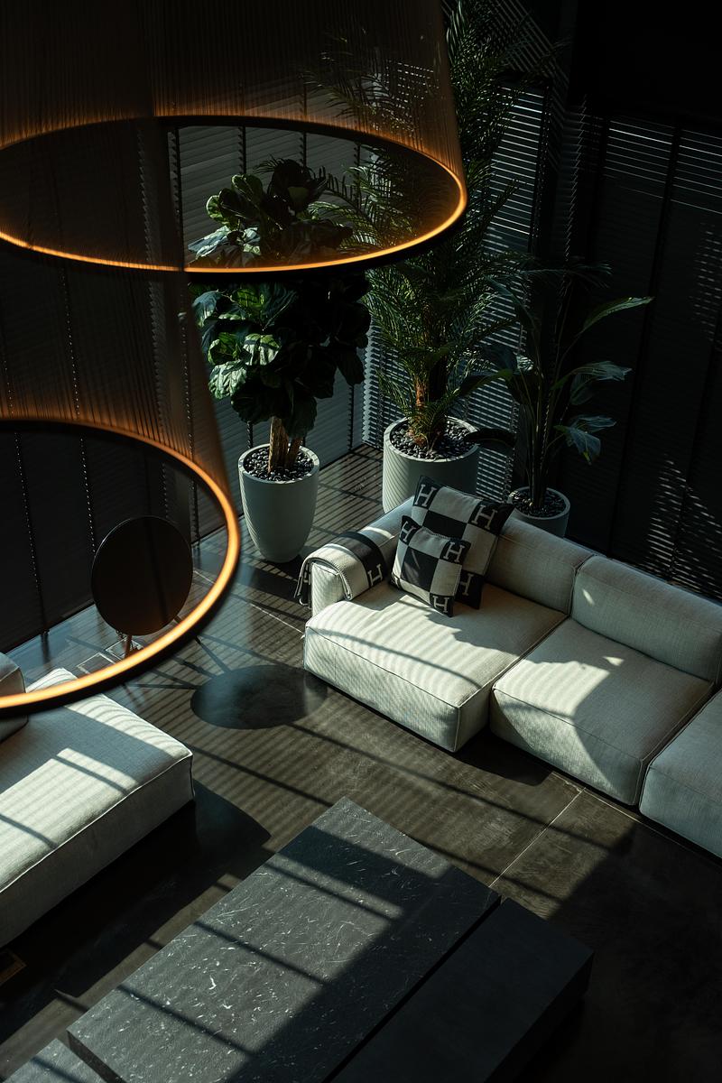 Salon de penthouse avec canapé clair, plantes d’intérieur et suspension circulaire design créant des jeux de lumière