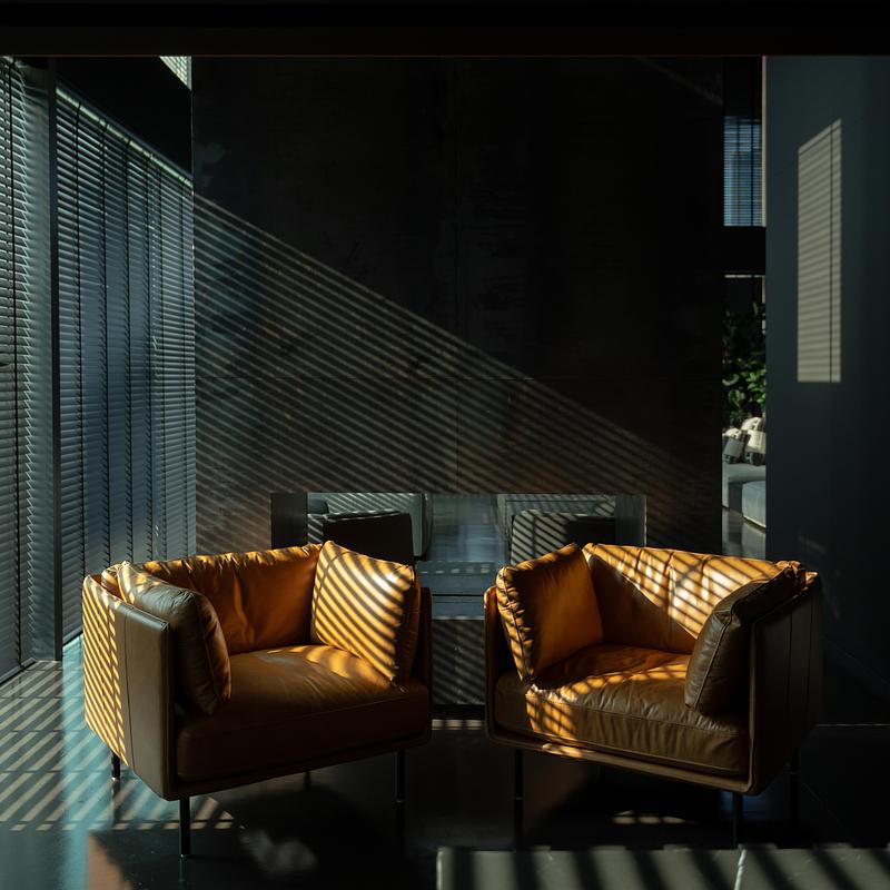 Fauteuils en cuir dans un intérieur minimaliste avec jeux d’ombres et de lumière naturelle filtrée par des stores