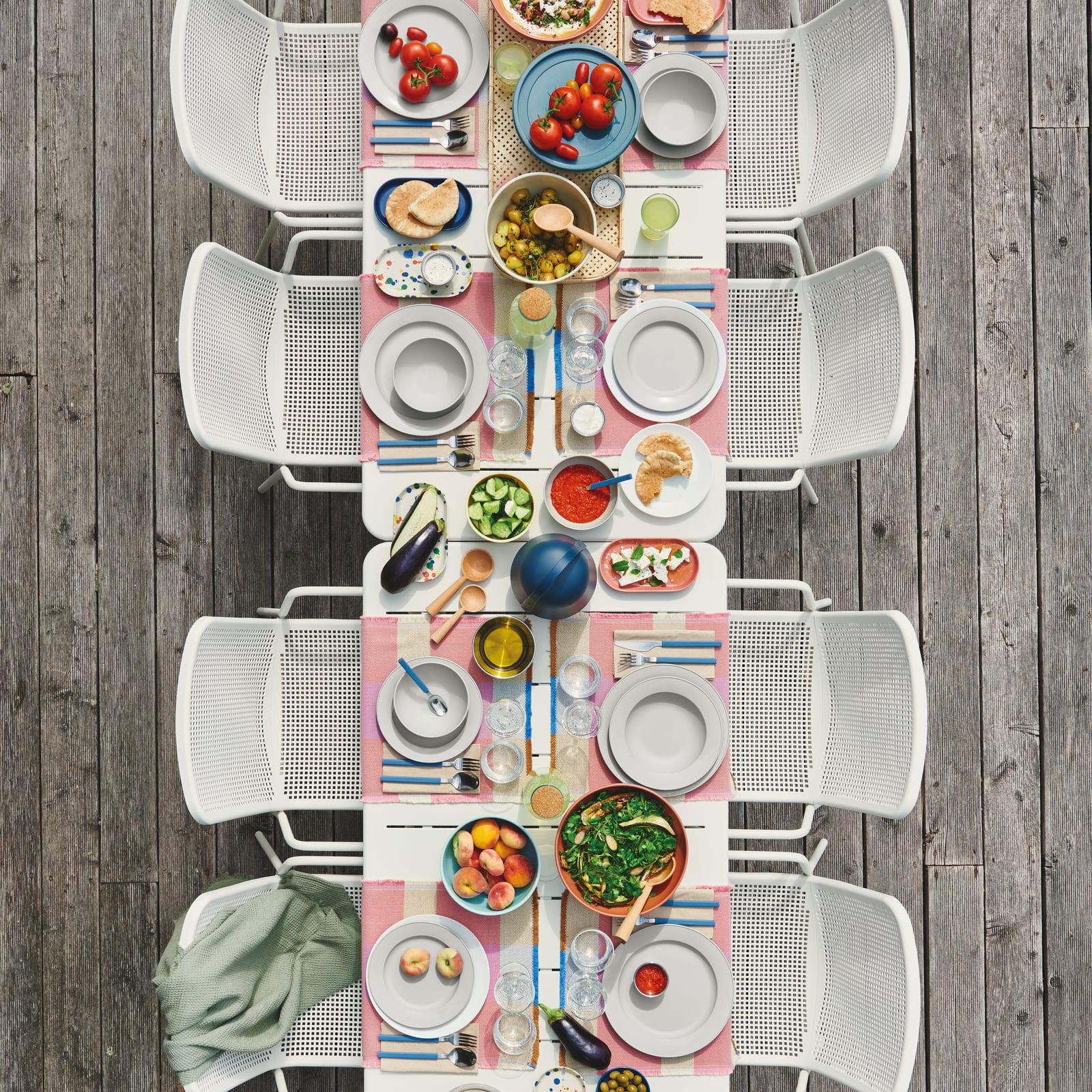 Grande table extérieure blanche vue de dessus, mets colorés, tomates, fenouil, olives et pêches dans un décor Fermob