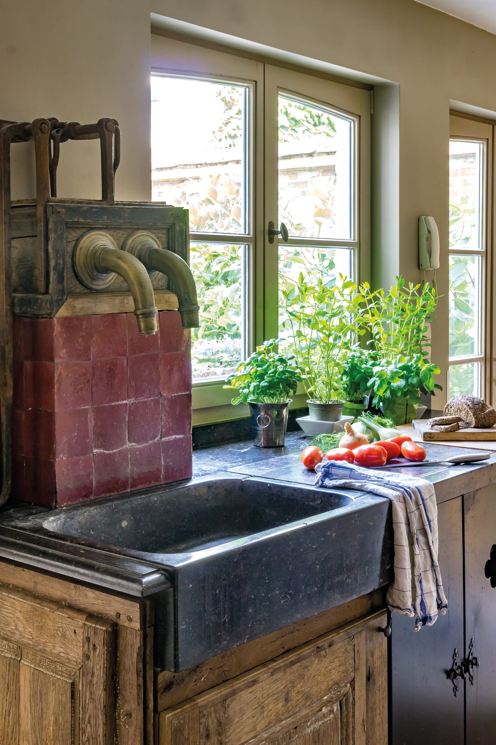 Évier timbre d'office en pierre bleue, robinetterie ancienne en laiton et carreaux de terre cuite dans une cuisine rustique