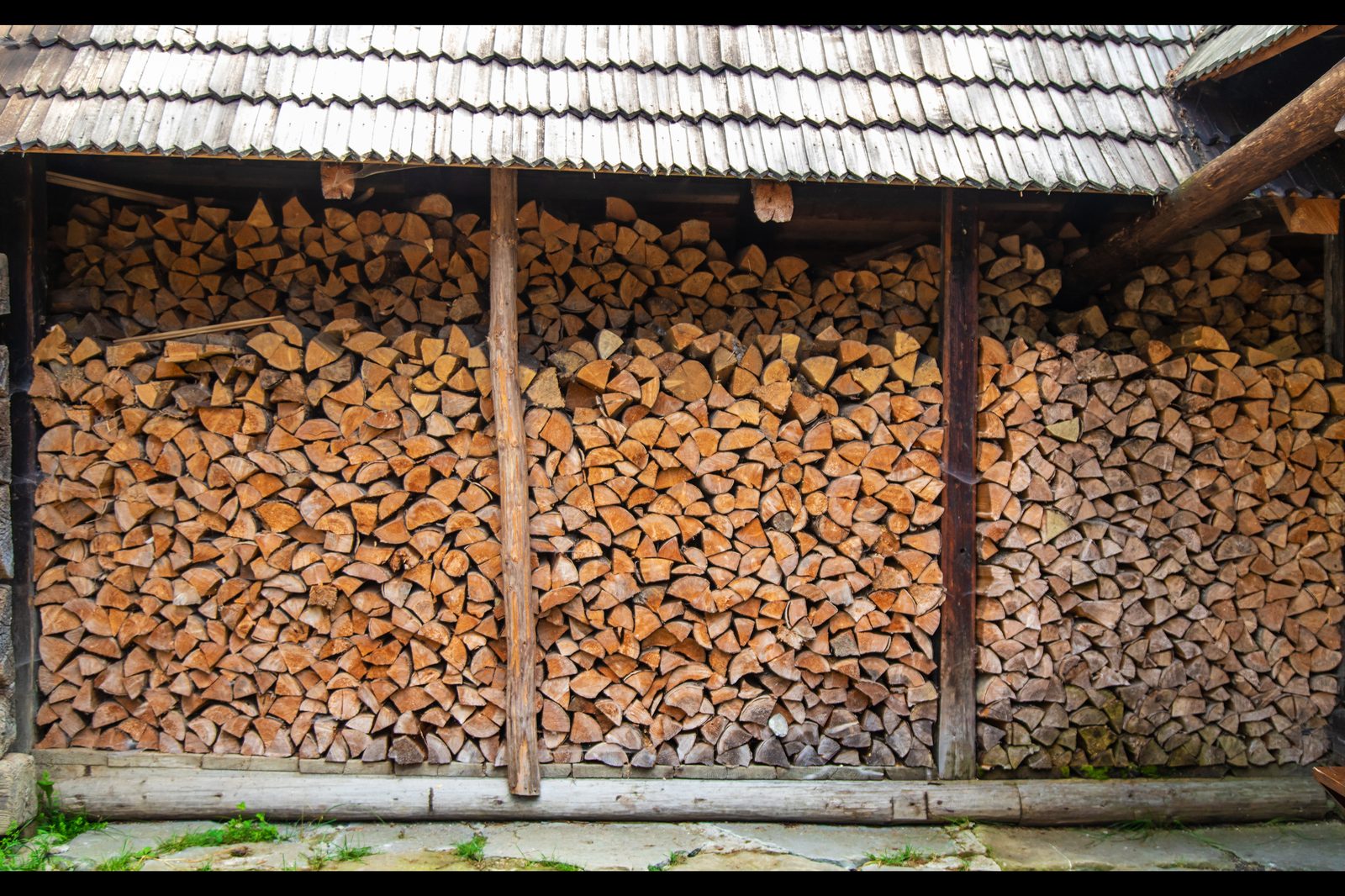 Abri pour stocker son bois de chauffage : bûches fendues empilées du sol au toit sous un toit de bardeaux, ouvert sur le devant