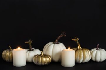 Décoration d’Halloween chic : citrouilles blanches et dorées et bougies blanches allumées sur fond noir