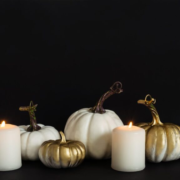 Décoration d’Halloween chic : citrouilles blanches et dorées et bougies blanches allumées sur fond noir