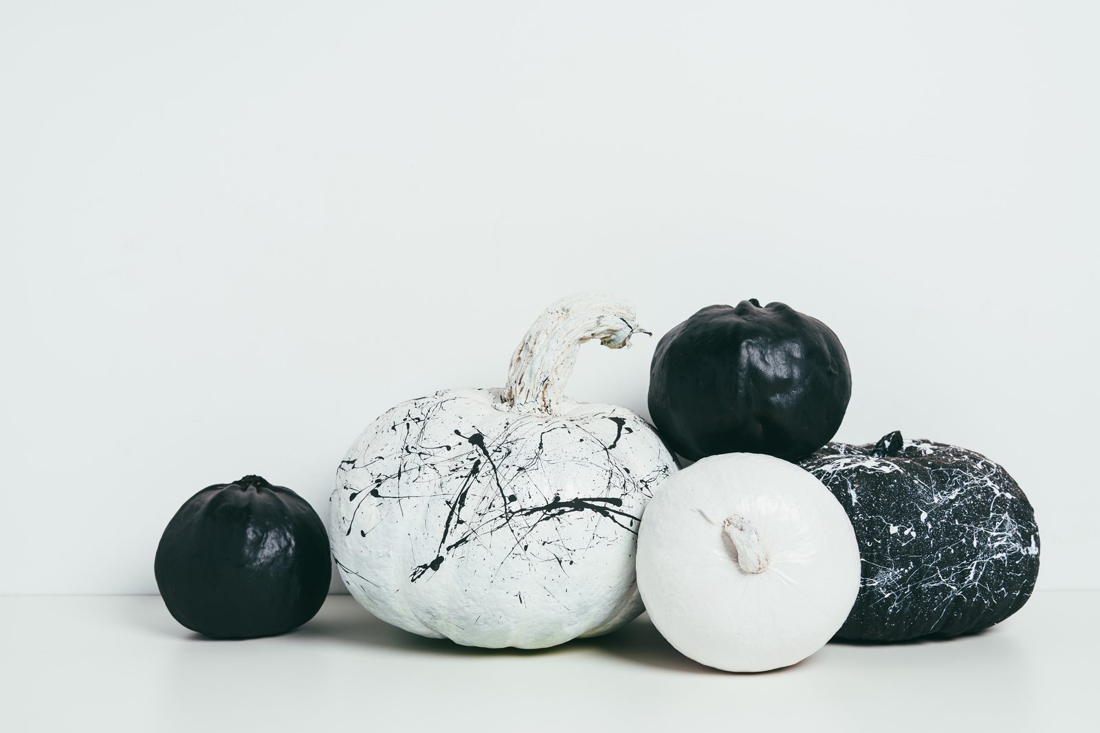 Citrouilles peintes en noir mat, en blanc et éclaboussées de peinture noire et blanche, posées sur une étagère blanche