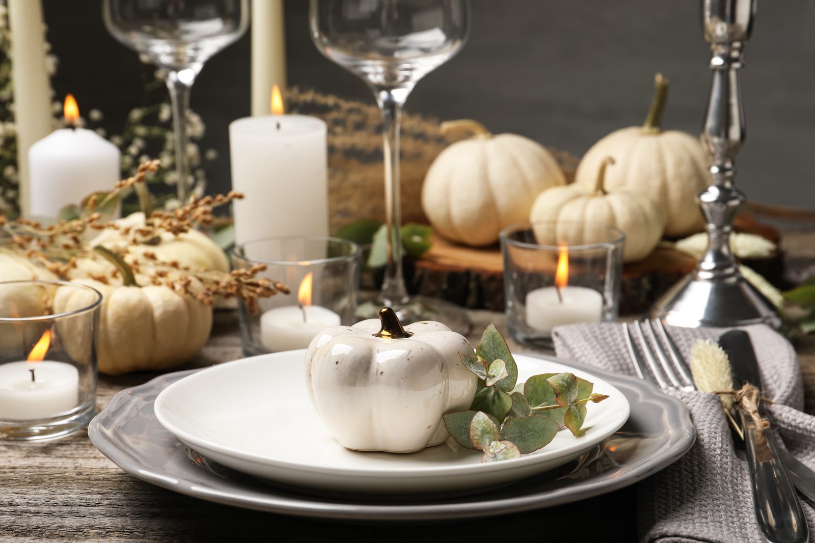 Table dressée pour l’automne : petite citrouille blanche posée sur une assiette avec une branche d’eucalyptus, bougies blanches, verres et citrouilles claires en arrière-plan