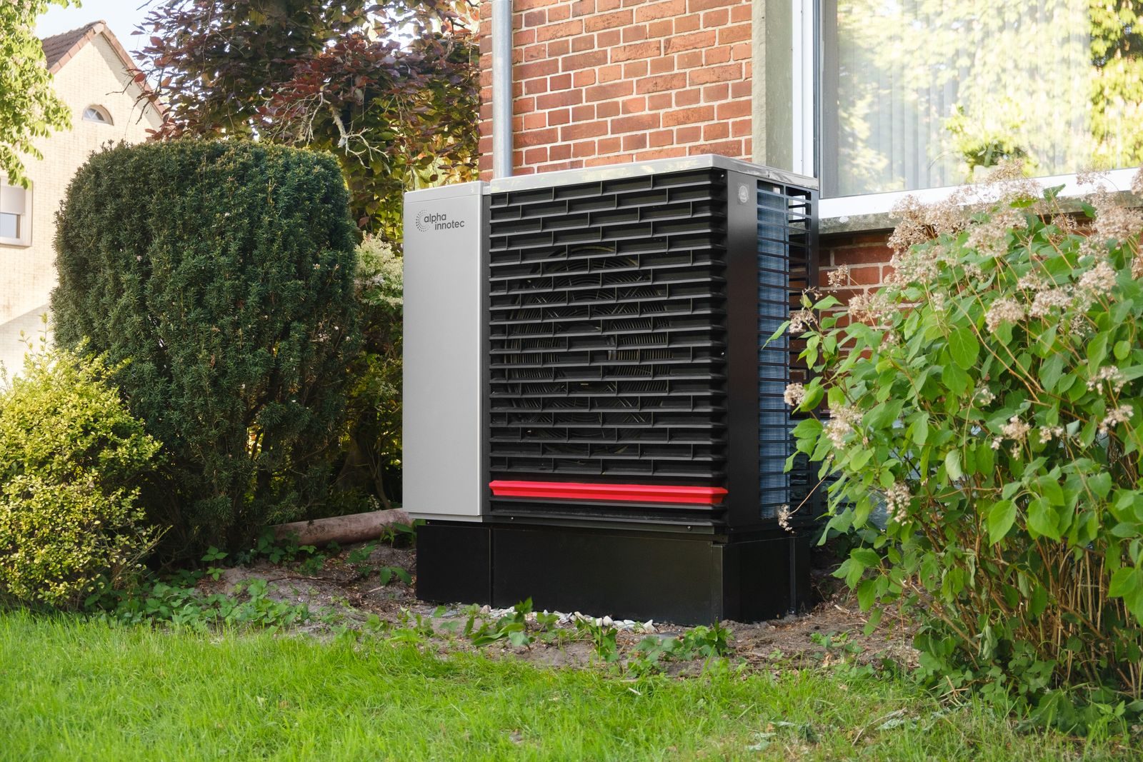 Unité extérieure d'une pompe à chaleur air/eau installée dans le jardin d'une maison en brique