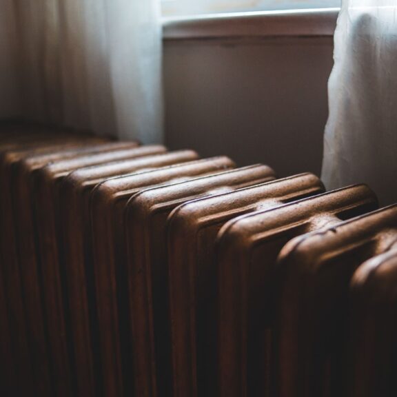 Radiateur ancien en fonte sous une fenêtre voilée de rideaux clairs, dans la lumière du jour