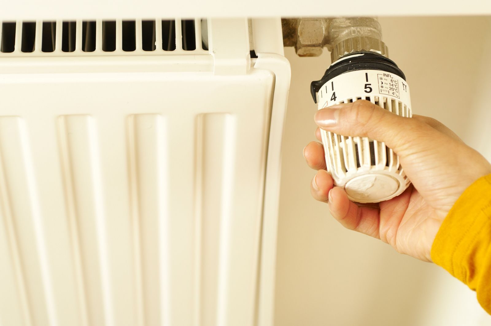 Main réglant le robinet thermostatique d'un radiateur à eau blanc