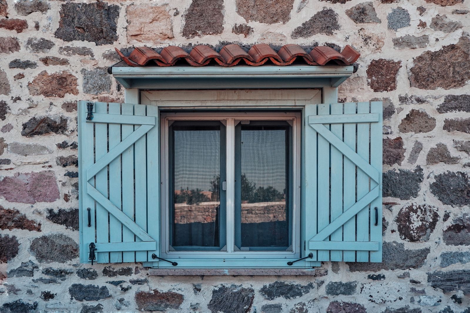 Fenêtre à volets battants en bois bleu sur une façade en pierre, sous un petit auvent de tuiles