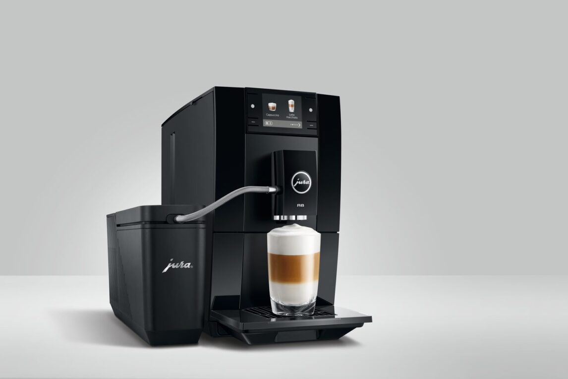 Machine à café automatique JURA A8 noire préparant un latte macchiato, reliée par un tuyau à un récipient à lait JURA, sur fond gris clair