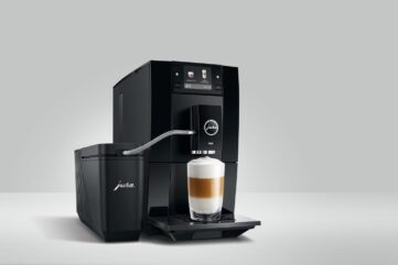 Machine à café automatique JURA A8 noire préparant un latte macchiato, reliée par un tuyau à un récipient à lait JURA, sur fond gris clair