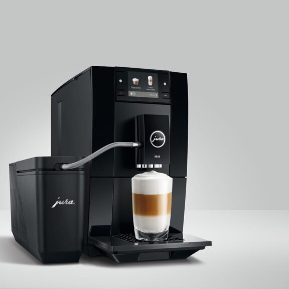 Machine à café automatique JURA A8 noire préparant un latte macchiato, reliée par un tuyau à un récipient à lait JURA, sur fond gris clair