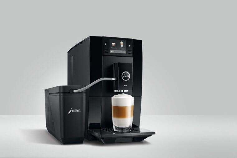 Machine à café automatique JURA A8 noire préparant un latte macchiato, reliée par un tuyau à un récipient à lait JURA, sur fond gris clair