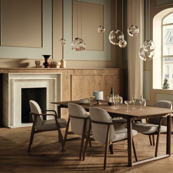 Salle à manger avec table en bois foncé configurable, chaises tapissées, cheminée en marbre et suspensions en verre