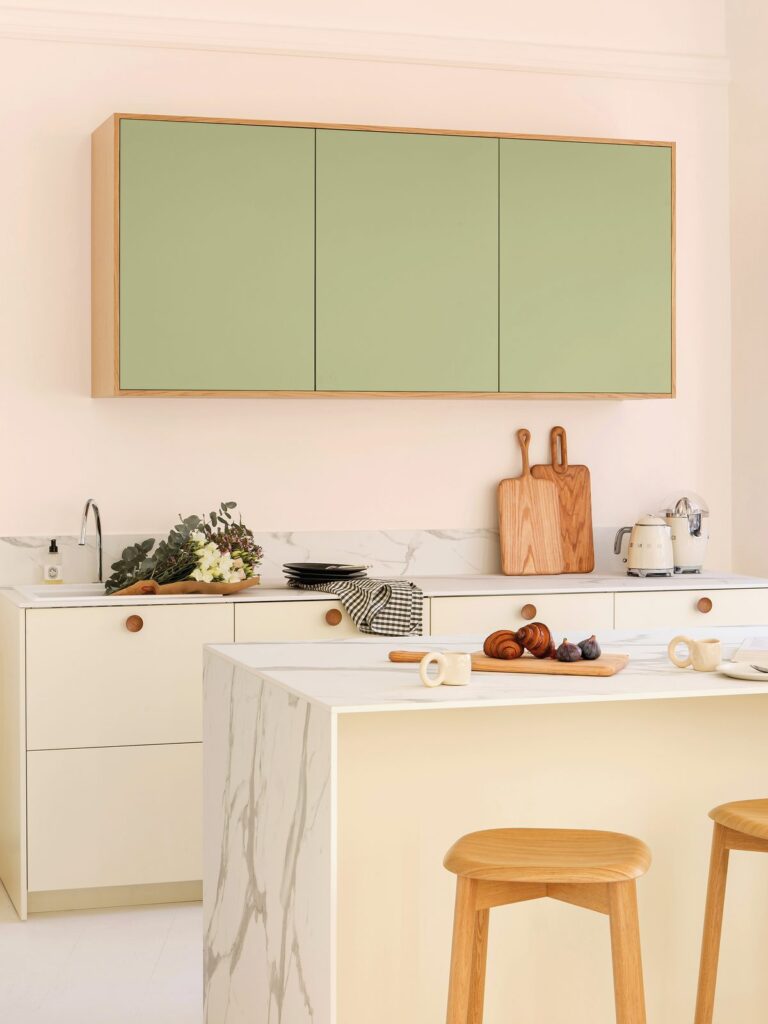 Cuisine aux façades crème et vert tilleul, îlot effet marbre et tabourets en bois clair