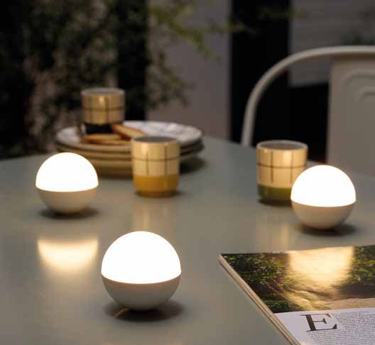 Trois petites boules lumineuses LED posées sur une table d'extérieur à côté de gobelets et d'un magazine