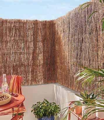 Balcon protégé par une canisse en brande de bruyère, avec table orange, plaid rayé et plantes vertes