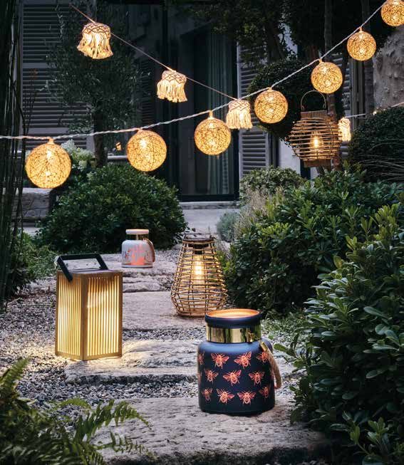 Allée de jardin éclairée le soir par une guirlande de boules tressées, des lanternes en bambou et des lampes nomades