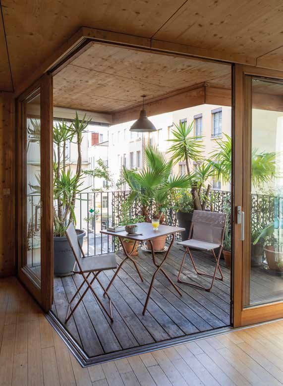 Loggia en bois ouverte sur un balcon avec table et chaises pliantes, palmiers et plantes en pots