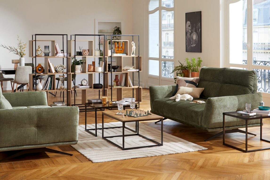 Grand séjour parisien avec canapés verts, tables basses en métal et bibliothèques ajourées en bois et métal séparant le coin repas