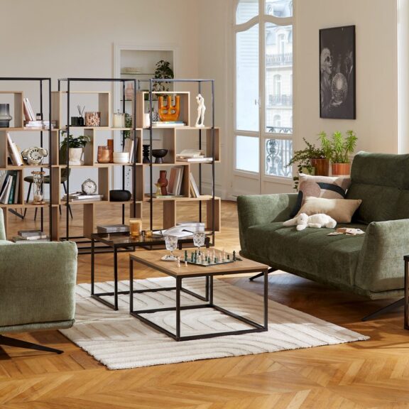 Grand séjour parisien avec canapés verts, tables basses en métal et bibliothèques ajourées en bois et métal séparant le coin repas