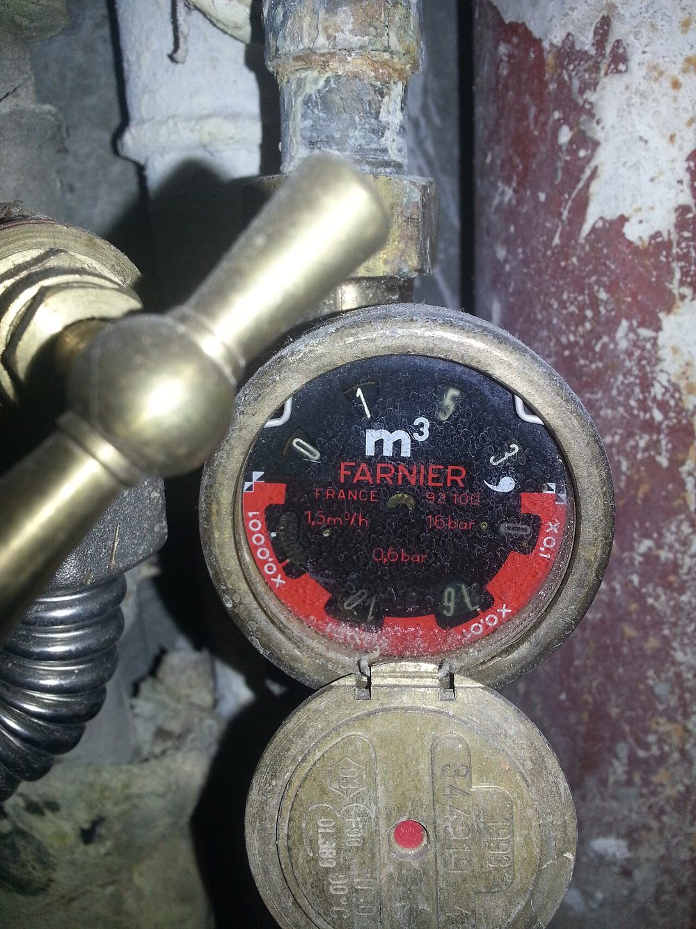 Ancien compteur d'eau Farnier en laiton, couvercle ouvert, à côté d'un robinet d'arrêt à poignée en laiton