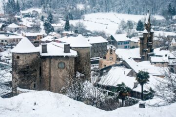 Toits enneigés du village de Seix en Ariège, avec son château aux tours rondes en pierre et le clocher de l'église