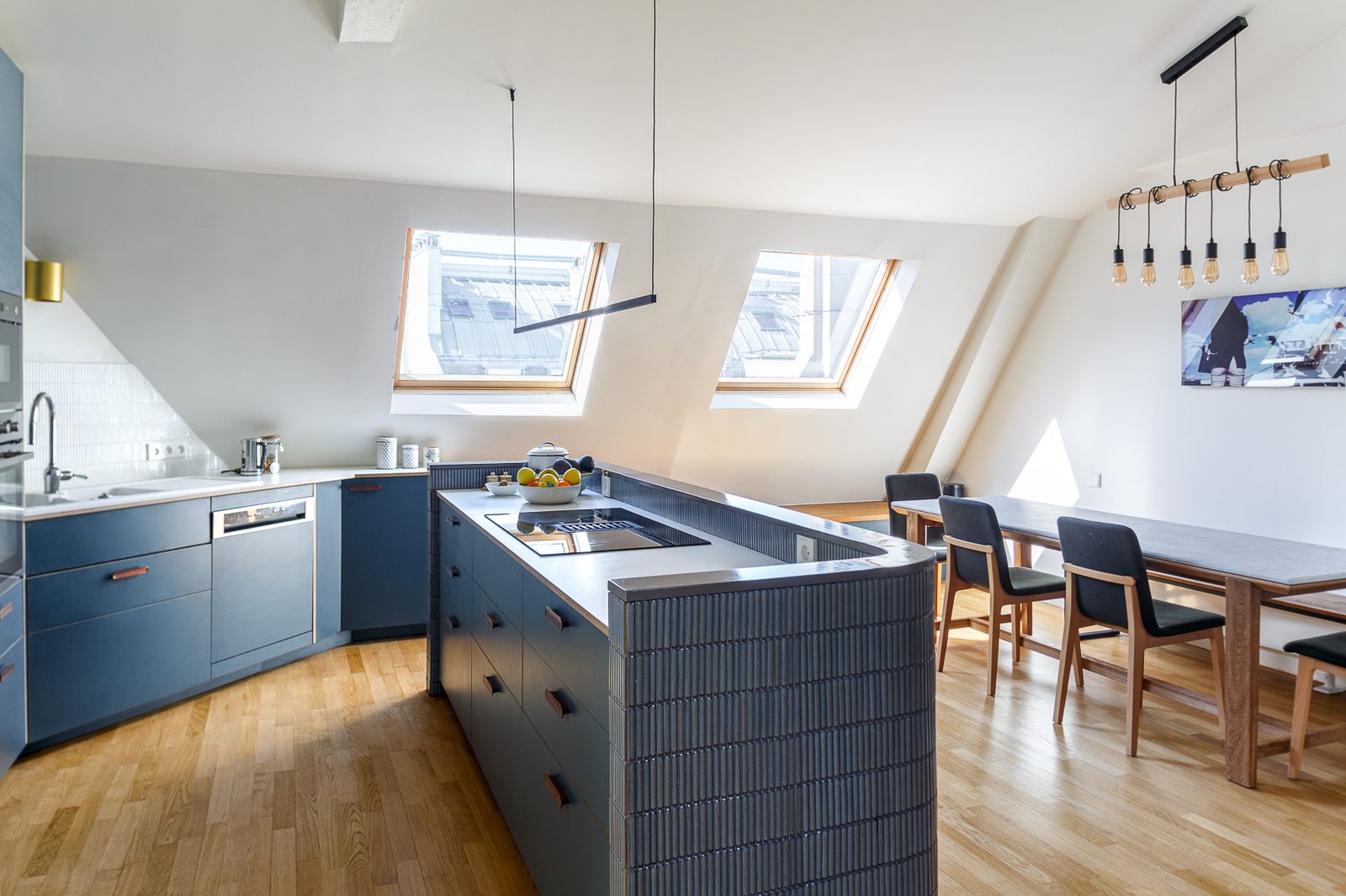 Cuisine sous combles avec îlot central bleu et fenêtres de toit