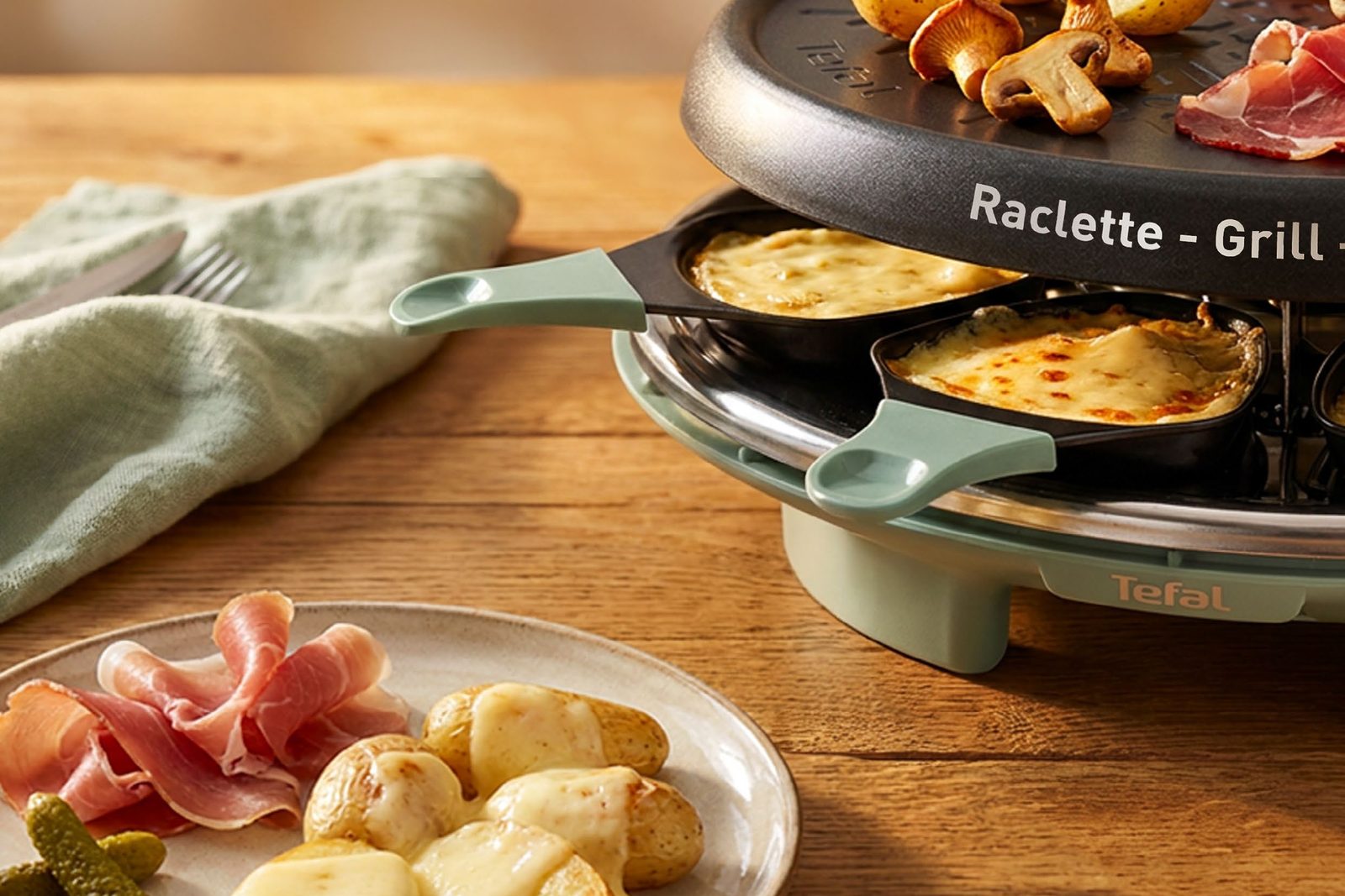 Plaque Raclette Grill Crêpe de la Tefal Raclette Célébration avec pommes de terre et champignons, deux poêlons gratinés au premier plan
