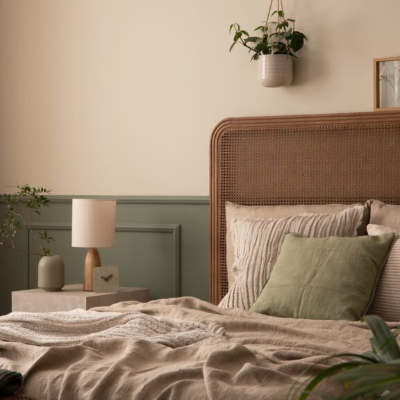 Aménager sa chambre pour mieux dormir : tête de lit en rotin, linge de lit en lin beige, coussin vert sauge et boiseries vert sauge